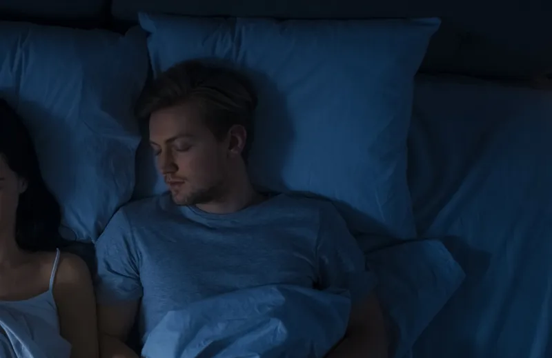 Two people asleep in a dark blue bedroom